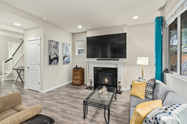 living room with a fireplace with flush hearth, stairway, baseboards, and wood finished floors