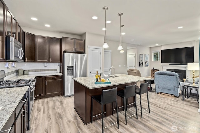 kitchen featuring a breakfast bar, light wood finished floors, appliances with stainless steel finishes, open floor plan, and dark brown cabinets