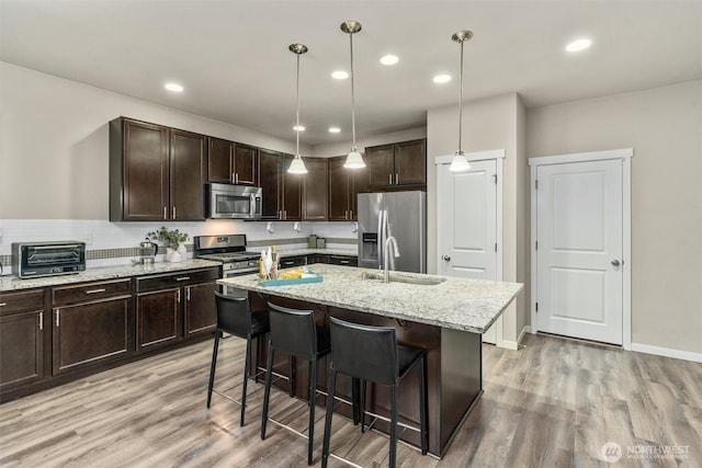 kitchen featuring dark brown cabinetry, a toaster, stainless steel appliances, a sink, and light wood-style floors