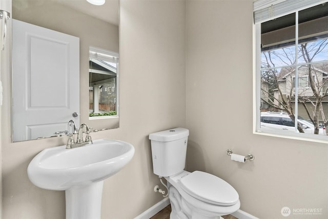 half bathroom with baseboards, a sink, and toilet