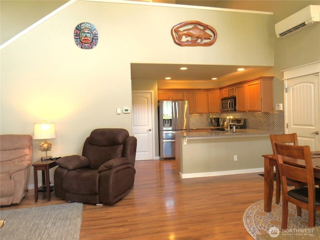 living room with an AC wall unit, wood finished floors, recessed lighting, baseboards, and a towering ceiling