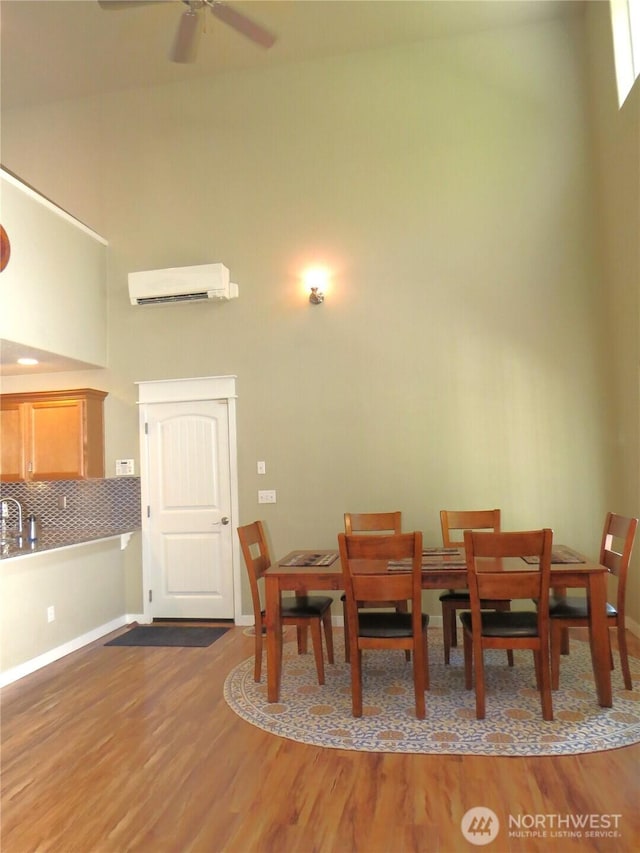 dining room with a ceiling fan, wood finished floors, baseboards, a high ceiling, and a wall mounted air conditioner