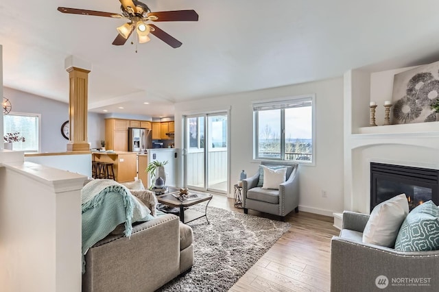 living room featuring ceiling fan, a glass covered fireplace, a healthy amount of sunlight, and light wood-style flooring