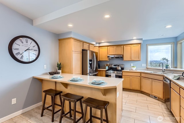 kitchen with a breakfast bar, light brown cabinetry, a sink, under cabinet range hood, and appliances with stainless steel finishes