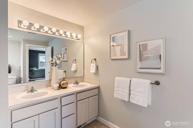 full bathroom featuring double vanity, toilet, baseboards, and a sink