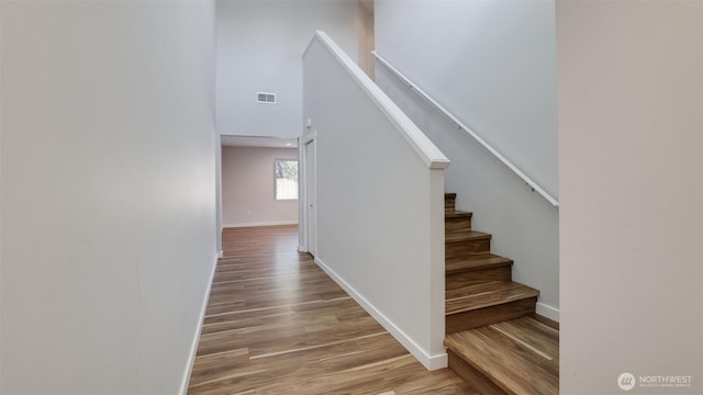 staircase featuring visible vents, a high ceiling, baseboards, and wood finished floors