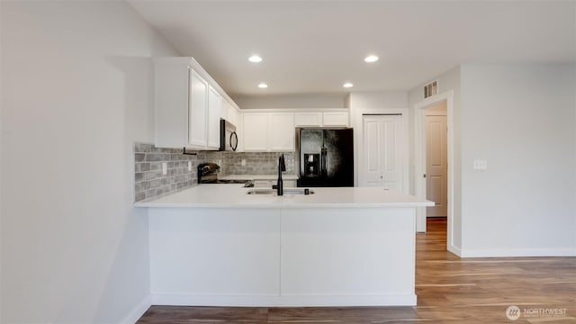 kitchen featuring visible vents, a peninsula, a sink, decorative backsplash, and black appliances