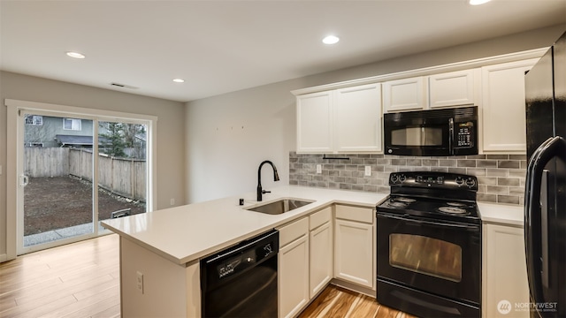 kitchen featuring black appliances, a sink, tasteful backsplash, a peninsula, and light countertops