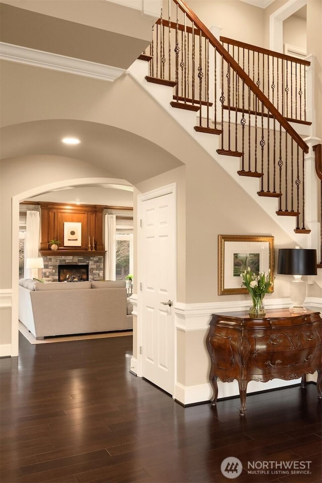 interior space with a stone fireplace, dark wood-type flooring, a towering ceiling, and ornamental molding