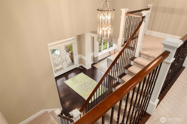 staircase with baseboards, wood finished floors, french doors, a towering ceiling, and an inviting chandelier
