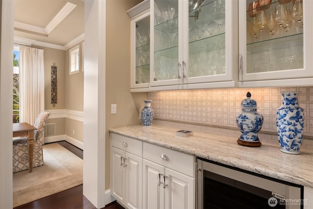 bar with backsplash, dark wood-type flooring, wine cooler, a tray ceiling, and ornamental molding