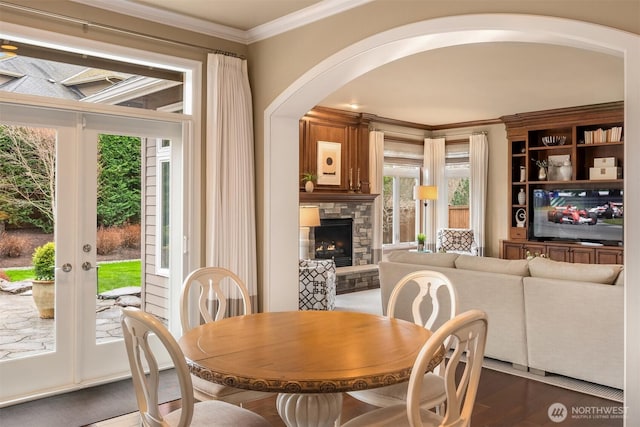dining room featuring french doors, dark wood-type flooring, a stone fireplace, and ornamental molding