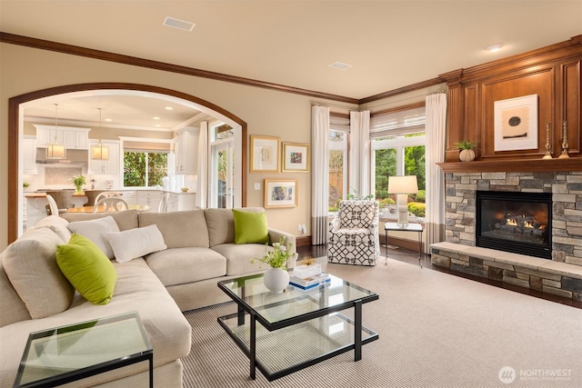 living area featuring arched walkways, plenty of natural light, a stone fireplace, and crown molding