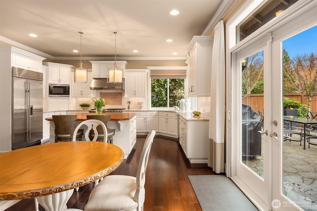 kitchen with backsplash, a kitchen island, under cabinet range hood, built in appliances, and white cabinetry