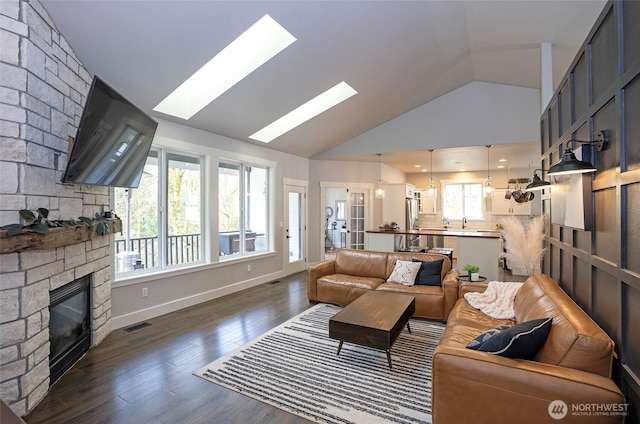 living area with wood finished floors, visible vents, baseboards, a stone fireplace, and lofted ceiling with skylight