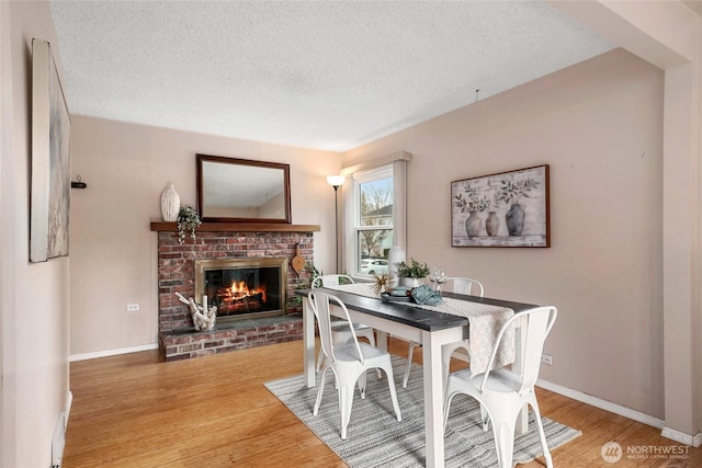 dining space featuring a brick fireplace, a textured ceiling, baseboards, and wood finished floors