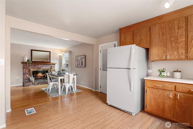 kitchen featuring light wood finished floors, light countertops, visible vents, freestanding refrigerator, and a brick fireplace