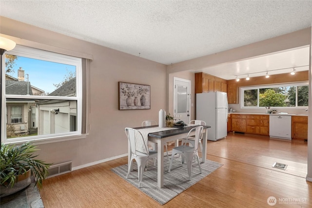 dining area featuring a textured ceiling, light wood finished floors, visible vents, and a healthy amount of sunlight