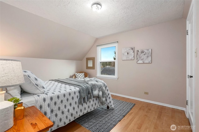 bedroom featuring vaulted ceiling, a textured ceiling, wood finished floors, and baseboards