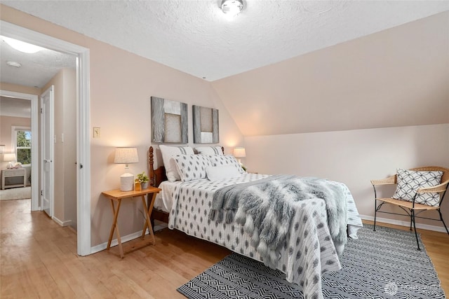 bedroom with lofted ceiling, a textured ceiling, baseboards, and wood finished floors