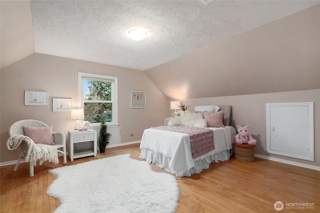 bedroom featuring light wood-type flooring, baseboards, a textured ceiling, and lofted ceiling