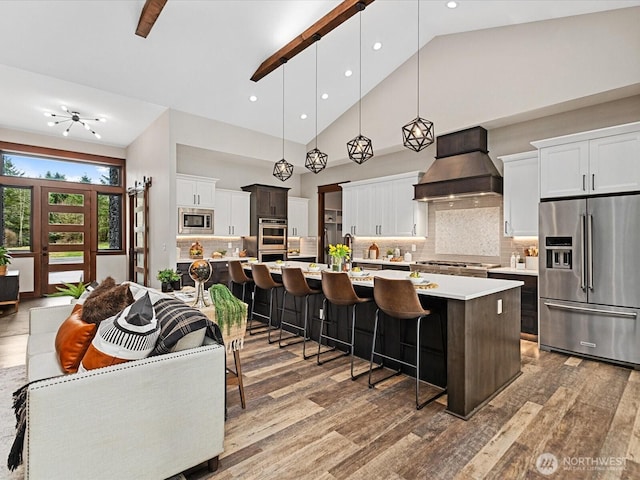 kitchen featuring wood finished floors, premium range hood, a large island with sink, stainless steel appliances, and light countertops