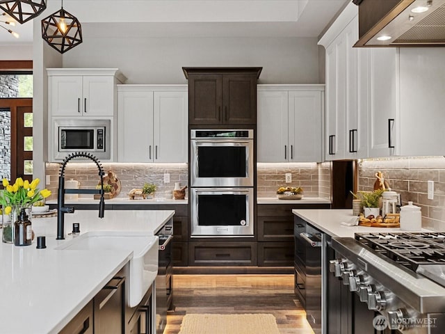 kitchen featuring stainless steel appliances, light countertops, wall chimney range hood, and a sink