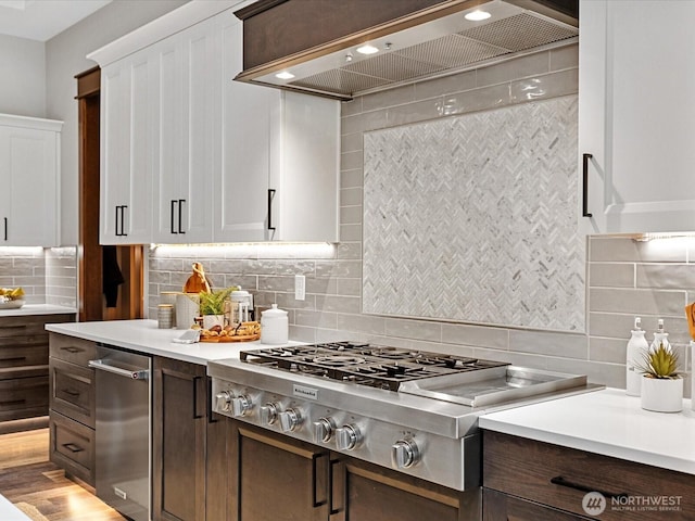 kitchen with backsplash, stainless steel gas stovetop, white cabinets, light countertops, and custom exhaust hood