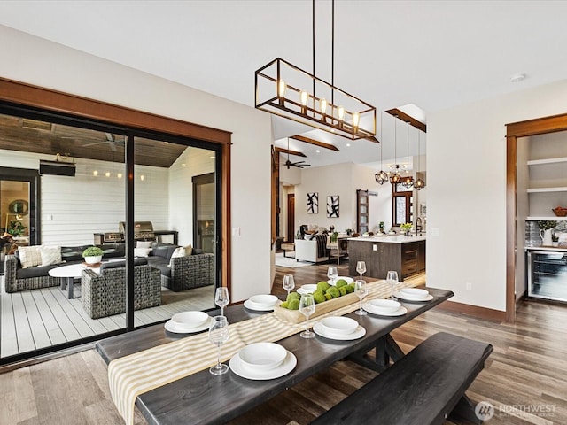 dining space with ceiling fan with notable chandelier, a dry bar, and wood finished floors