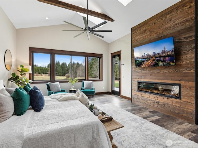 bedroom with beam ceiling, access to outside, wood finished floors, a glass covered fireplace, and baseboards