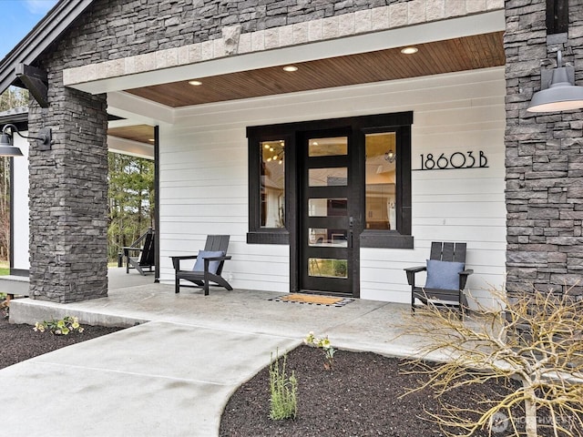 view of exterior entry featuring covered porch and stone siding