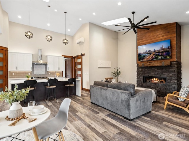 living area featuring wood finished floors, a skylight, a high ceiling, a stone fireplace, and an AC wall unit