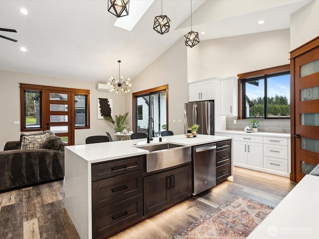 kitchen with a kitchen island with sink, a sink, stainless steel appliances, white cabinets, and light countertops