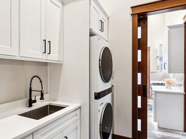 laundry area with cabinet space, stacked washing maching and dryer, and a sink