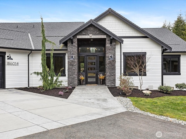 entrance to property with driveway, french doors, stone siding, and roof with shingles