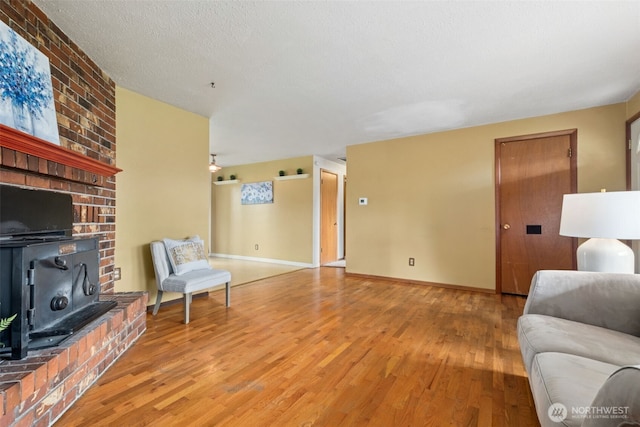 living area featuring a textured ceiling, a wood stove, baseboards, and wood finished floors