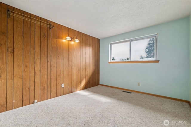 unfurnished room featuring visible vents, a textured ceiling, wooden walls, carpet, and baseboards