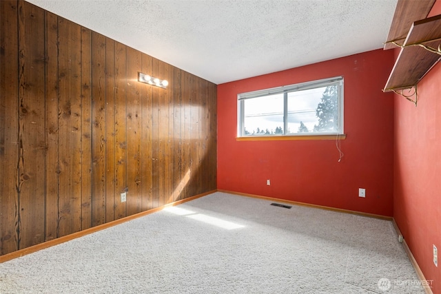 carpeted empty room featuring visible vents, wood walls, a textured ceiling, and baseboards