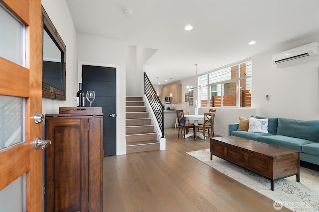 living room featuring wood-type flooring, a wall mounted air conditioner, an inviting chandelier, stairs, and recessed lighting