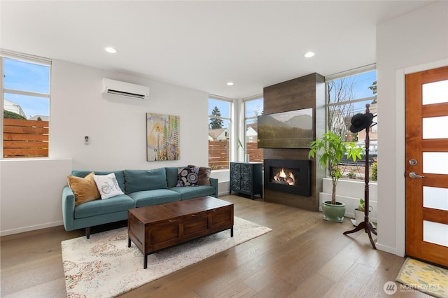 living room with an AC wall unit, wood finished floors, and a healthy amount of sunlight