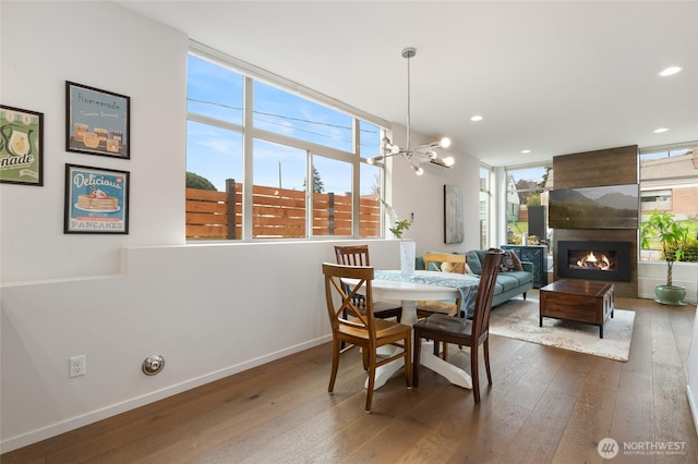 dining room featuring a large fireplace, baseboards, dark wood finished floors, and a chandelier