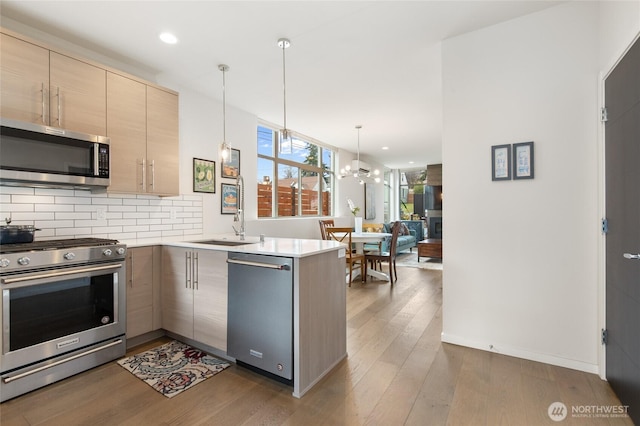 kitchen featuring stainless steel appliances, a peninsula, wood finished floors, light brown cabinetry, and tasteful backsplash