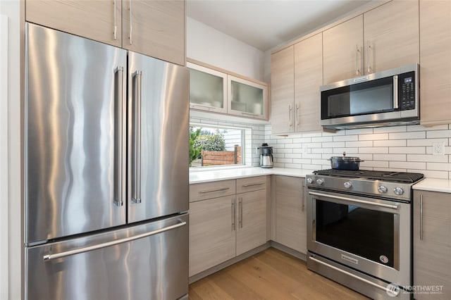 kitchen with light wood-style floors, appliances with stainless steel finishes, light countertops, and decorative backsplash