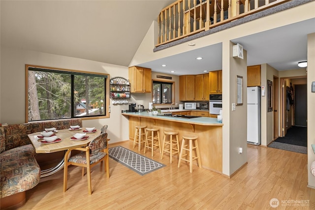 kitchen with white appliances, a breakfast bar area, a peninsula, light countertops, and light wood-style floors