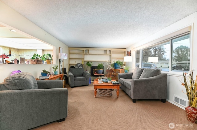 living room featuring carpet, visible vents, a textured ceiling, and a glass covered fireplace