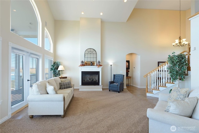 carpeted living area with a towering ceiling, an inviting chandelier, stairway, and a glass covered fireplace