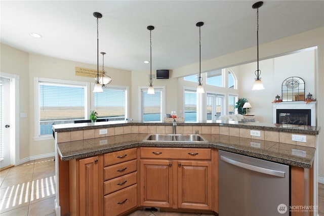 kitchen featuring a sink, hanging light fixtures, tile counters, dishwasher, and a glass covered fireplace