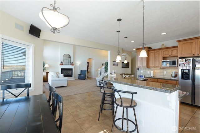 kitchen featuring arched walkways, tasteful backsplash, appliances with stainless steel finishes, light tile patterned flooring, and a kitchen breakfast bar