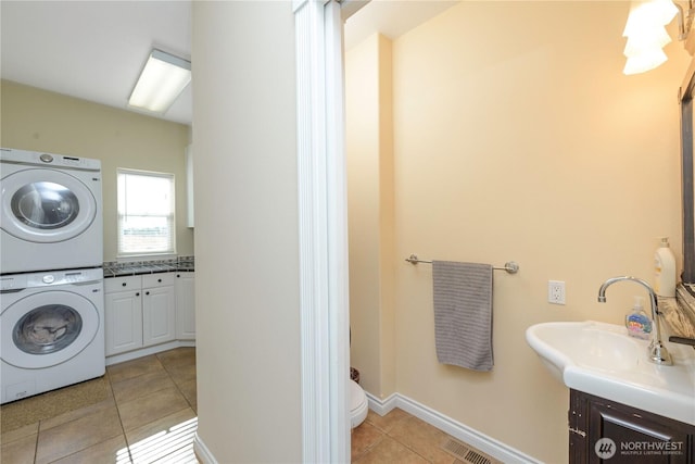 laundry area featuring laundry area, visible vents, stacked washer / drying machine, a sink, and light tile patterned flooring
