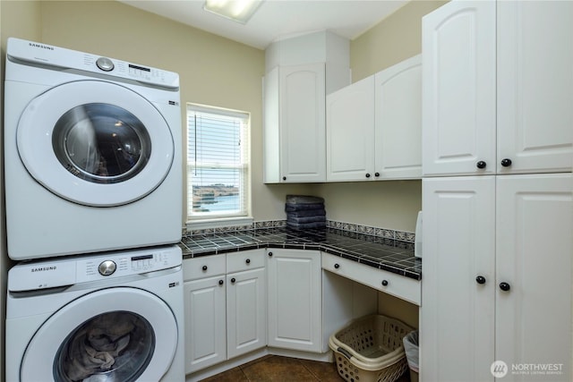 washroom with dark tile patterned flooring, cabinet space, and stacked washing maching and dryer